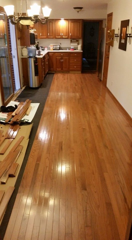 Hardwood floor extending from kitchen, cabinets visible in the background, a work area with wood planks on the left.