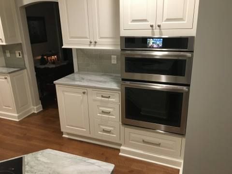 White kitchen cabinetry with stainless steel double oven, marble countertops, and hardwood floors.