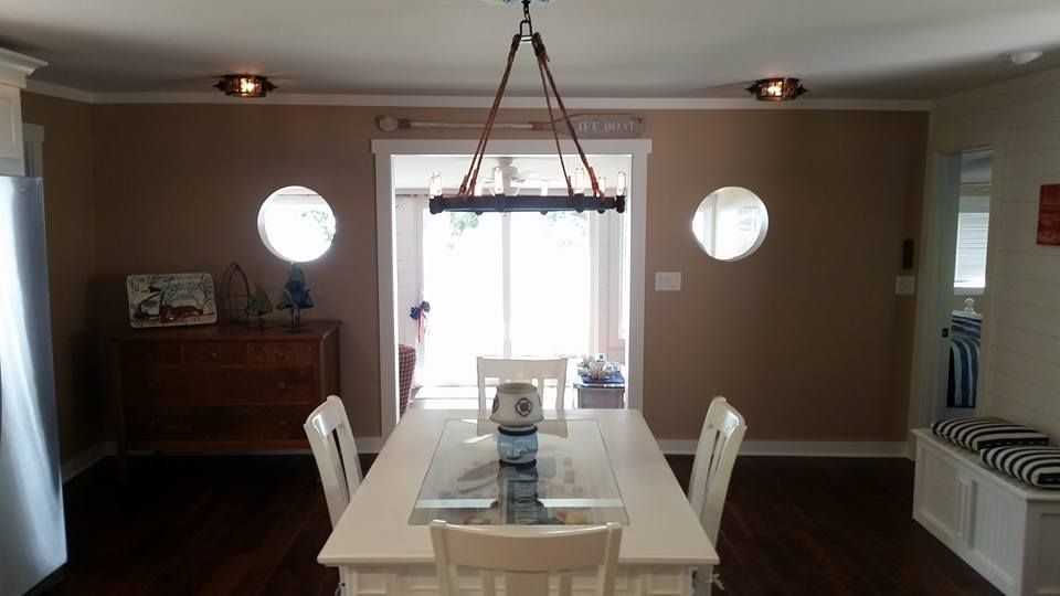 Dining room with white table and chairs, dark wood floor, tan walls, porthole windows, and chandelier.