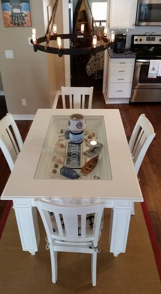 White dining table with glass center, set with seashells and a robot. Four white chairs sit around it.