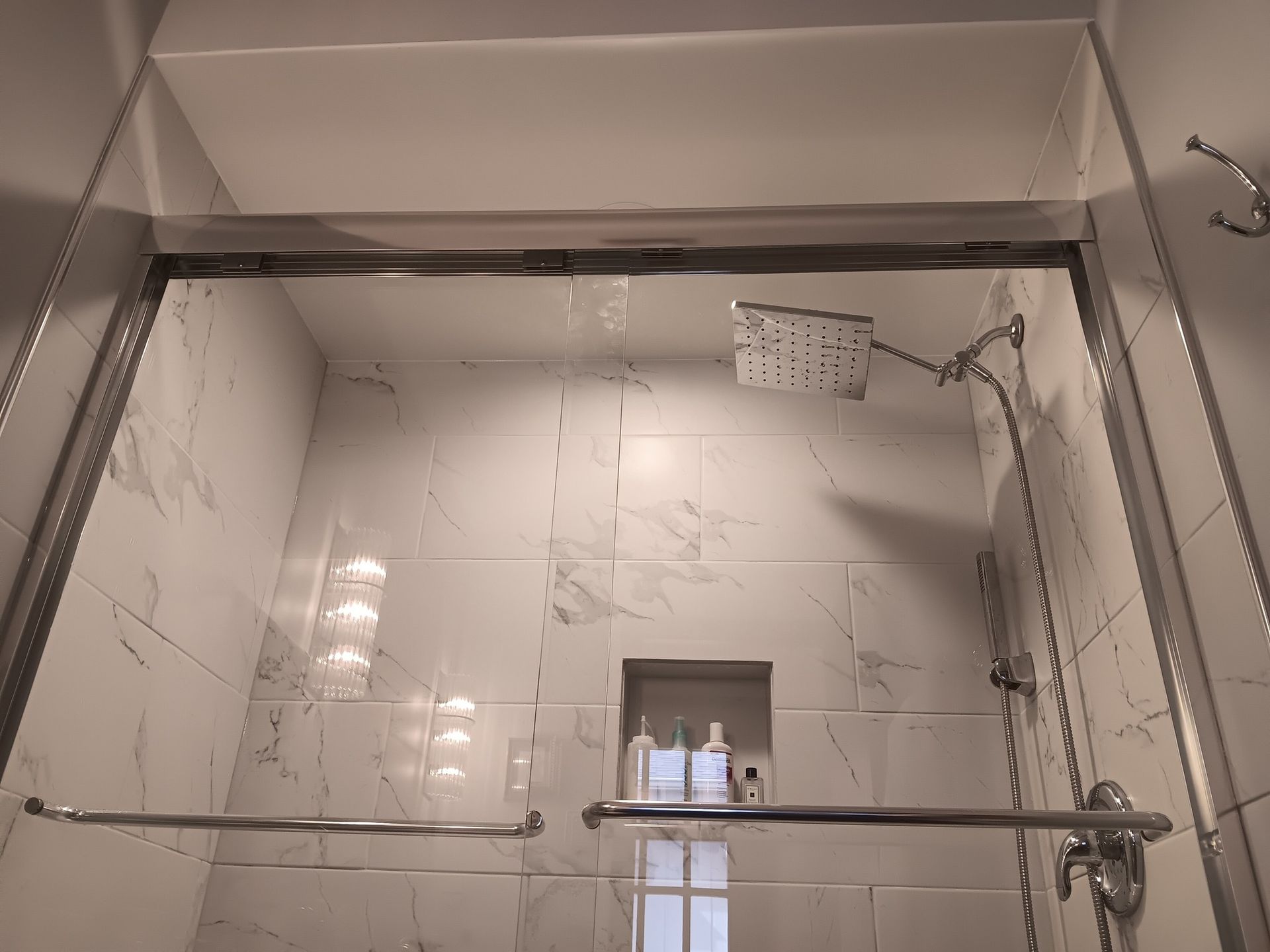 Shower with glass doors and white marble tile. A shower head is visible.