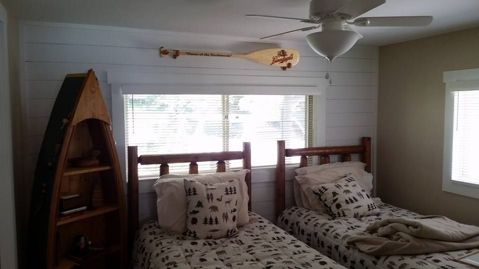 Bedroom with two twin beds, decorative canoe, and oar above the window. Whitewashed accent wall.