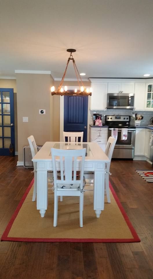 Dining room with white table and chairs, brown wood floor, blue door, white cabinets, and wooden chandelier.