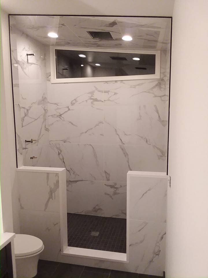 Modern shower with white marble-look tiles, a glass enclosure, and a small window above.
