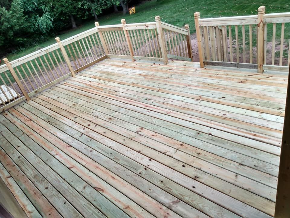 Wooden deck with railings and steps leading down to a yard with green grass.