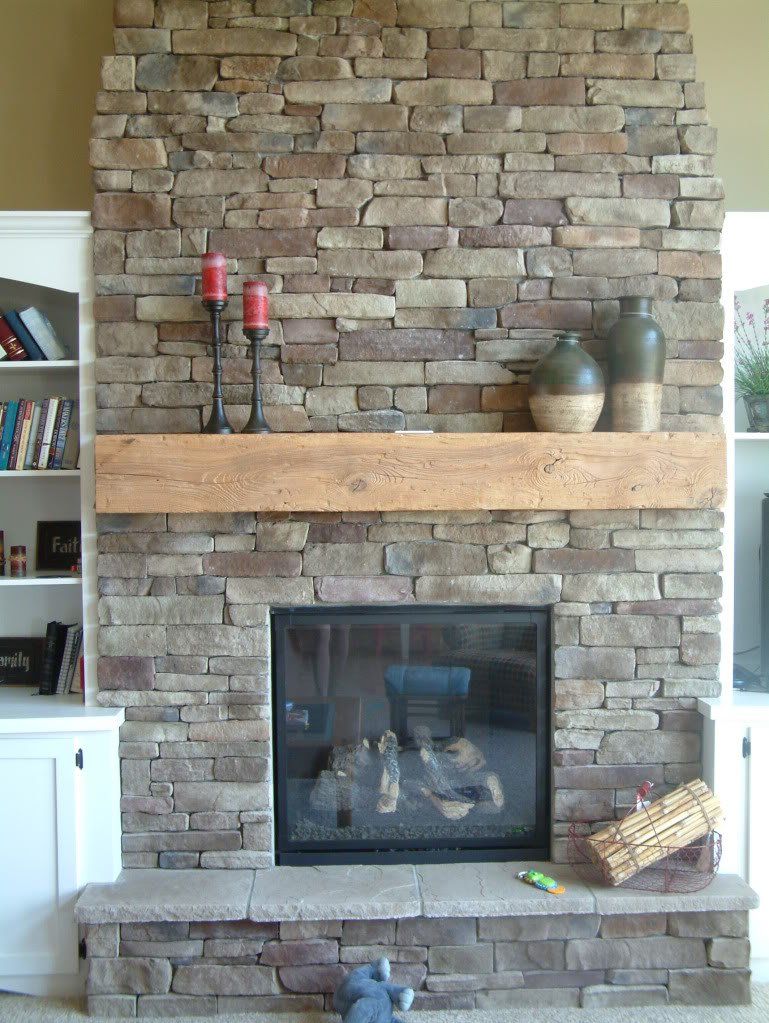 Stone fireplace with wooden mantel, flanked by white built-in shelves.