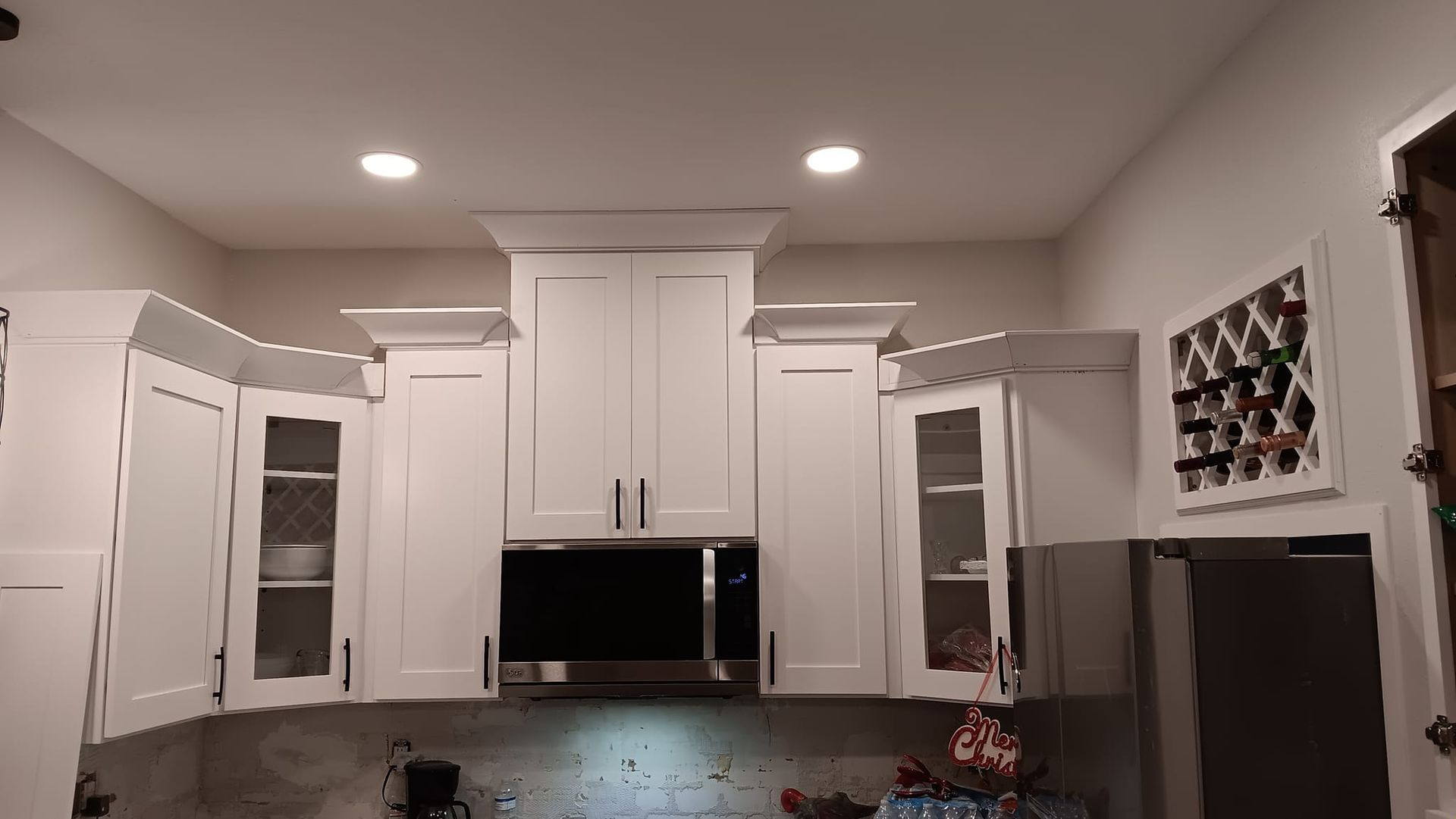 White kitchen cabinets with microwave, wine rack, and refrigerator.
