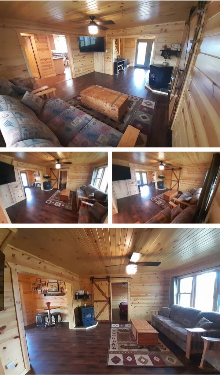 Rustic cabin interior with wood-paneled walls, hardwood floors, and comfortable seating, including a sofa and a loveseat.