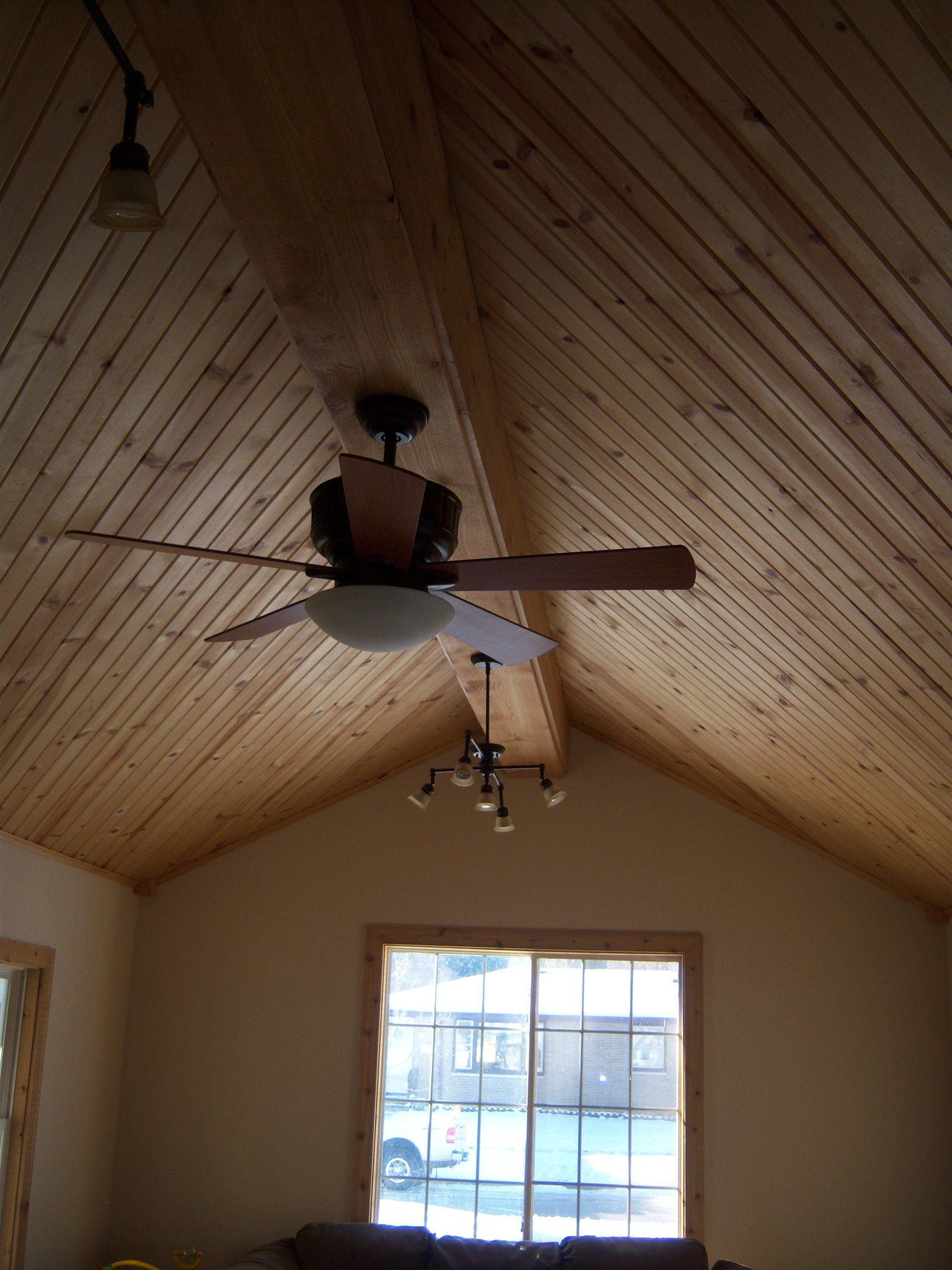 Angled wood-paneled ceiling with a ceiling fan and a window at the end.