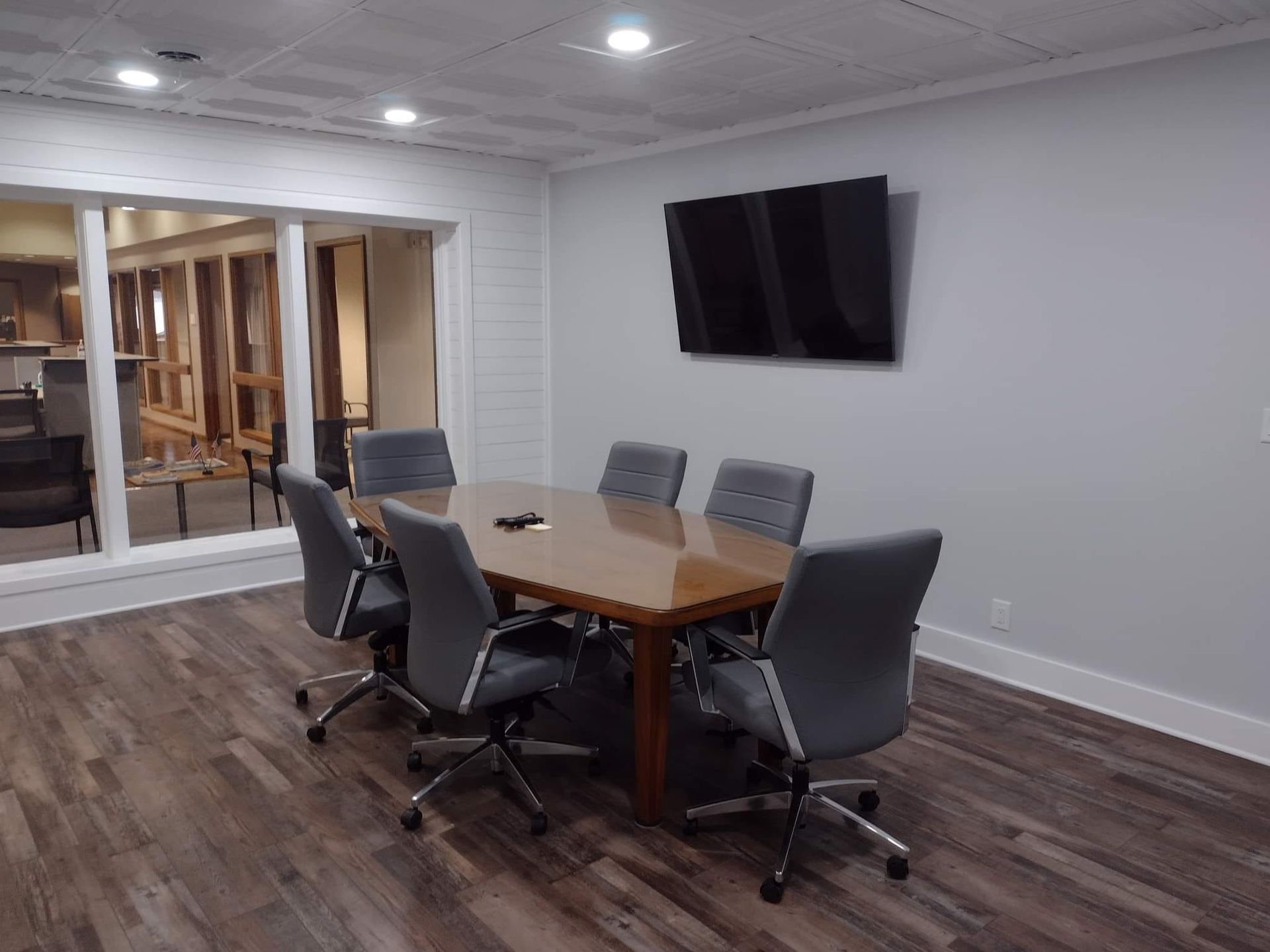 Meeting room with a rectangular table, gray chairs, and a wall-mounted TV.