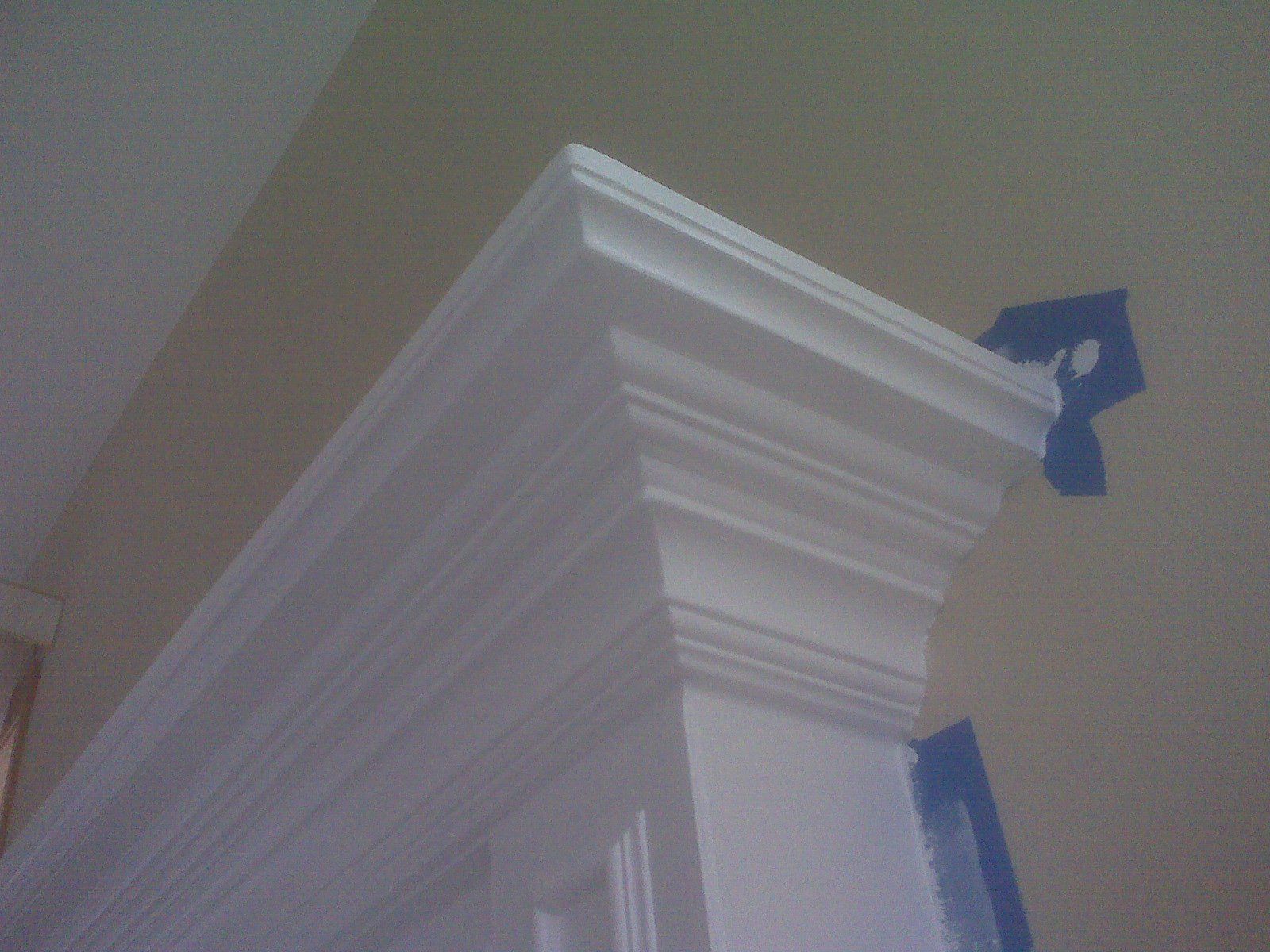 White painted crown molding against a beige wall, with blue painter's tape visible.