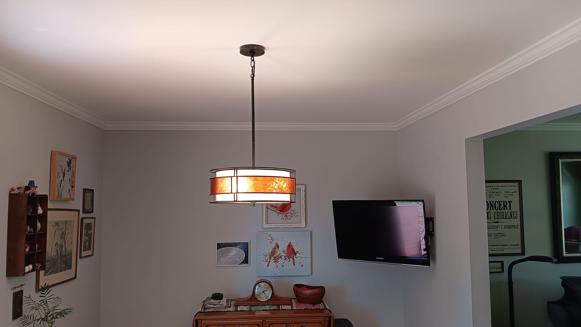 A pendant light hangs over a dining area. Artwork and a TV are on the wall.