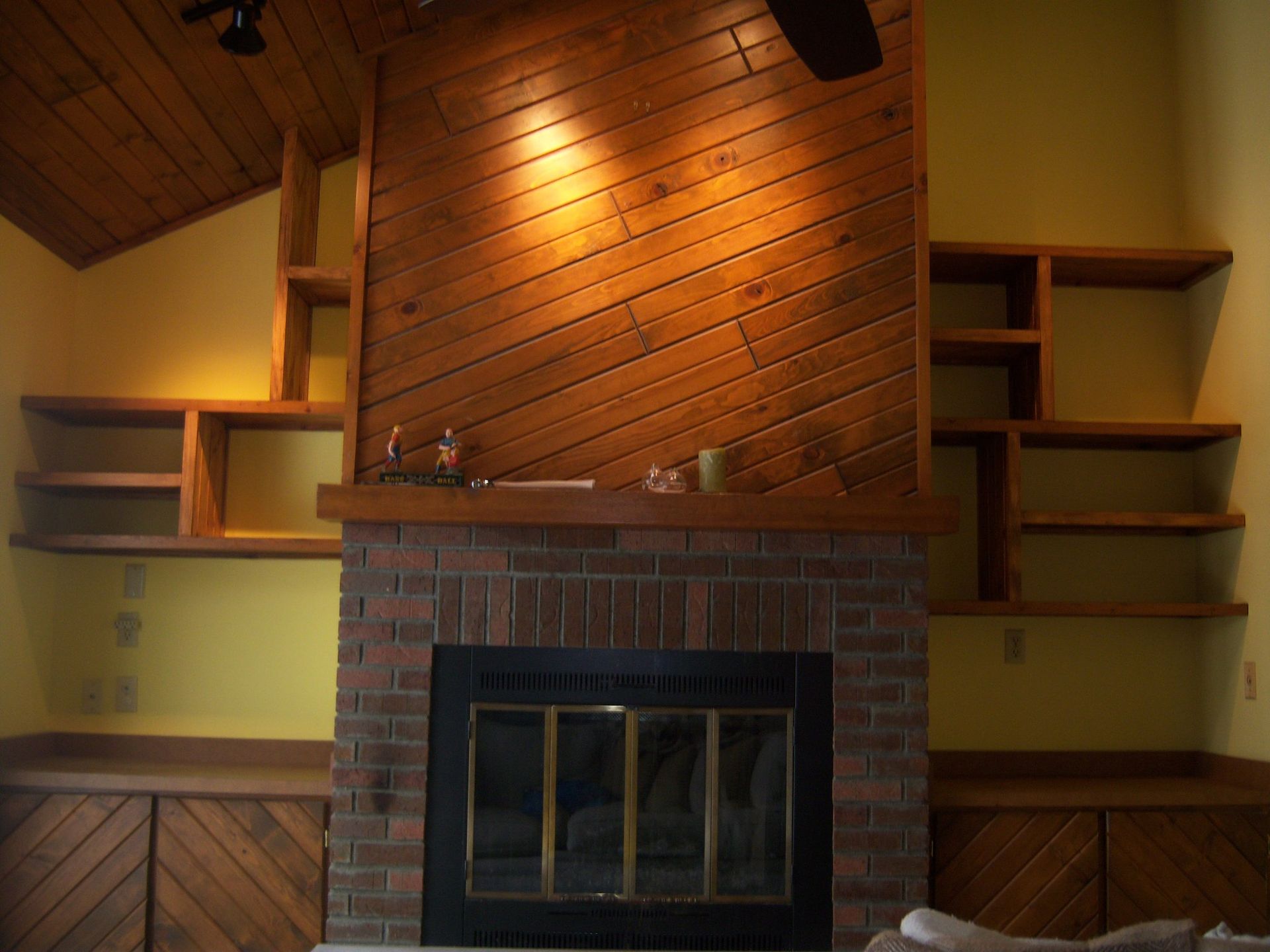 Fireplace with brick surround, built-in wooden shelves and cabinetry on yellow walls.