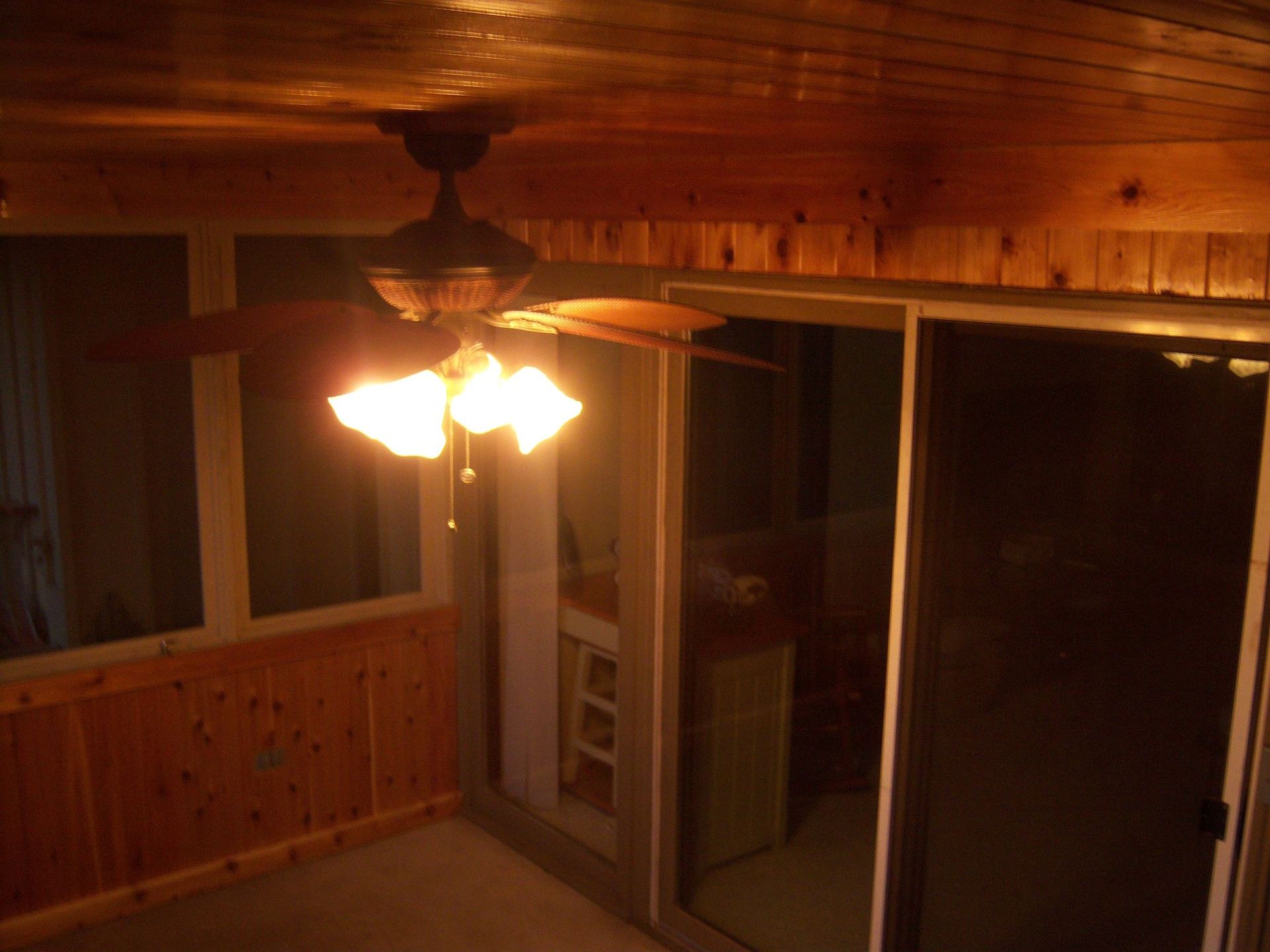 Sunroom with wood paneling, sliding glass door, and ceiling fan with lights.