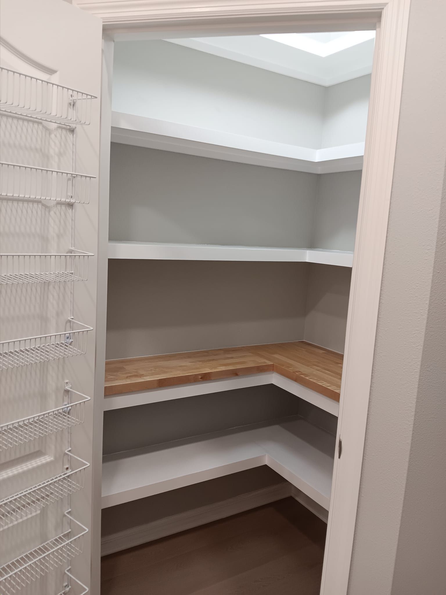 Empty pantry with built-in shelves. One shelf has a butcher block countertop. Open door on the left side.