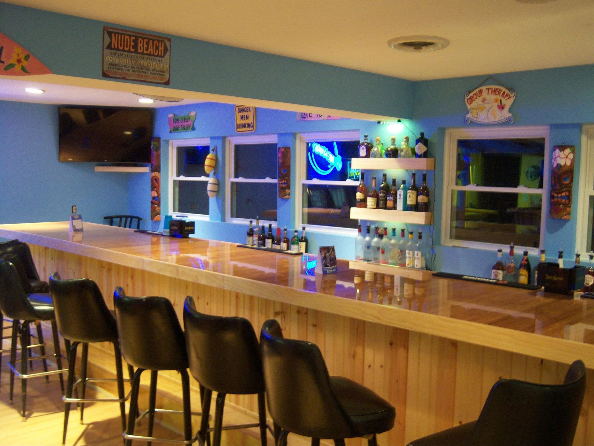 Bar with wooden facade, stools, bottles on shelves, and a blue wall.