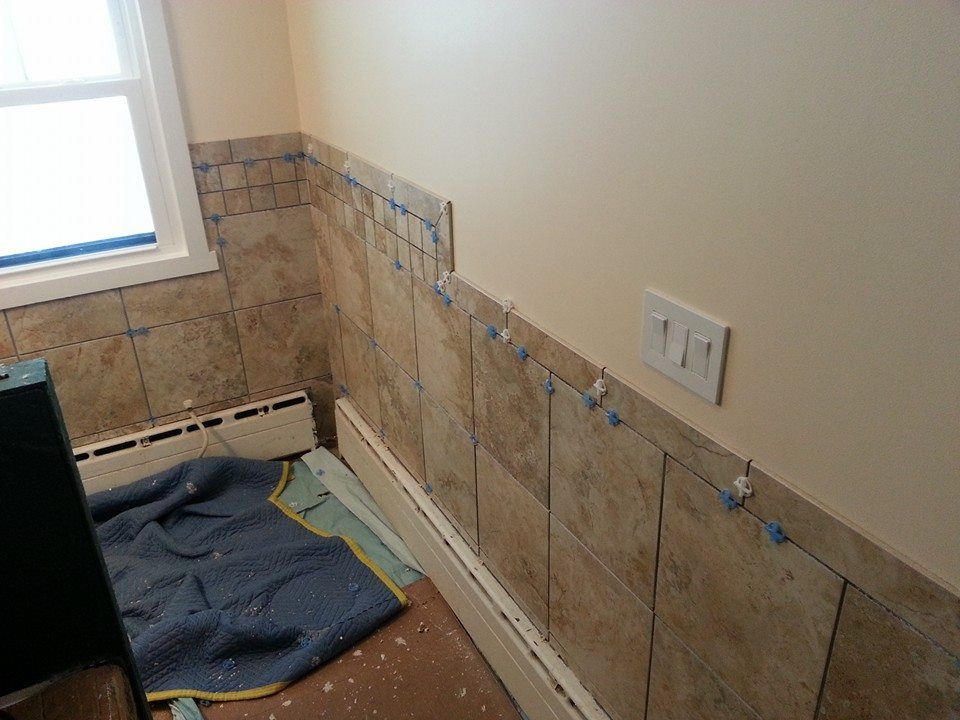 Bathroom with tan tile being installed on the wall. Window on left, light switch on right.