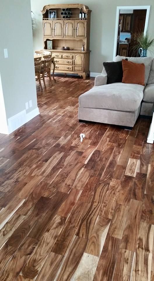 Hardwood floor in a living room with a beige sectional, wooden cabinet, and dining area.