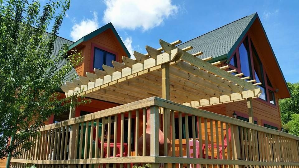 Wooden deck with pergola attached to a two-story orange-brown cabin under a blue sky.