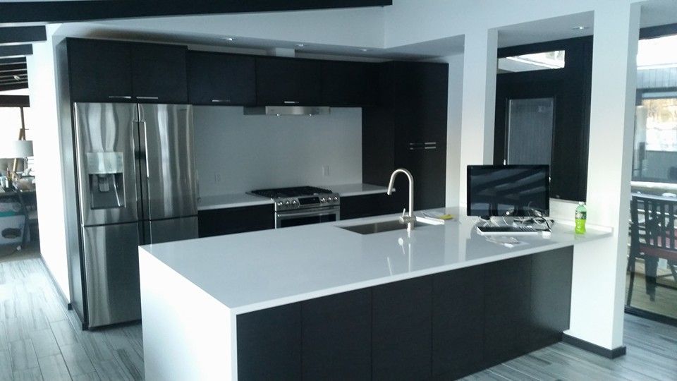 Modern kitchen with stainless steel appliances, dark cabinets, and white countertop island.