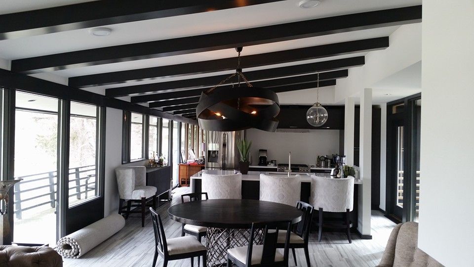 Modern dining room with black beams, table, and chairs. Large windows, kitchen island, and decorative light fixture.