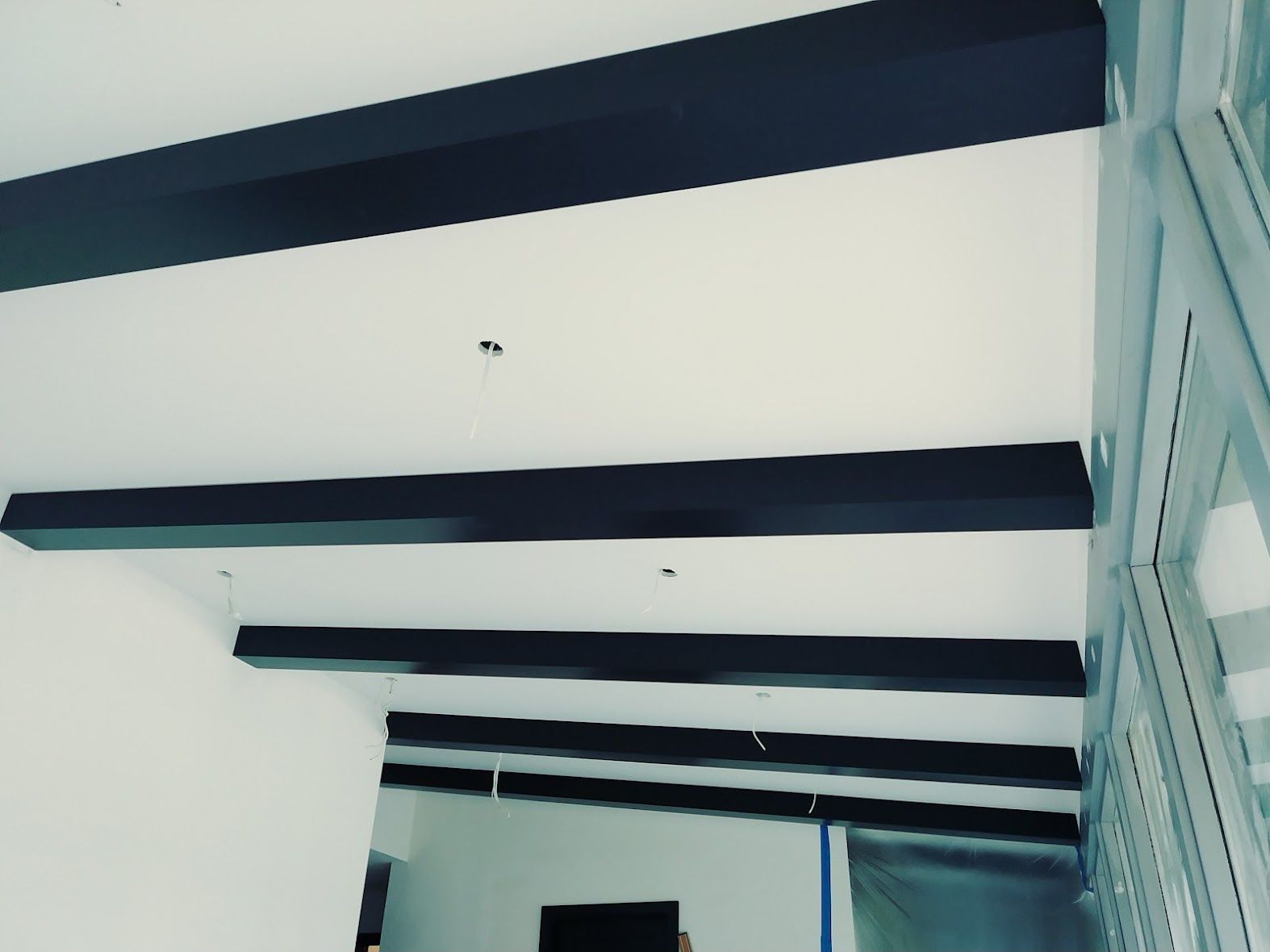 Black beams on a white ceiling. Interior view with a doorway on the bottom left and a window on the right.