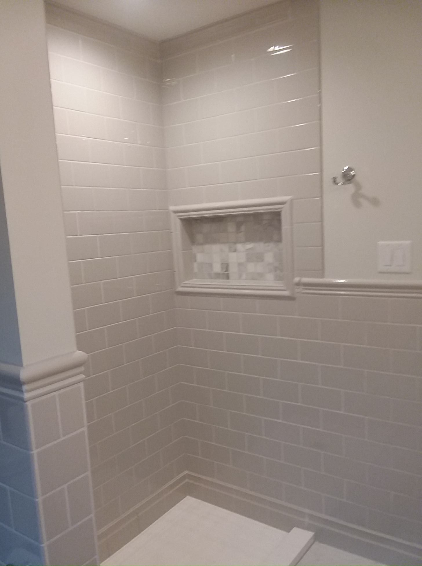 Gray tiled shower with recessed shelf, white trim, and a towel bar.