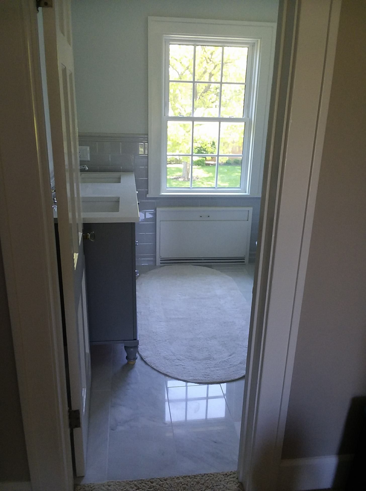 Bathroom doorway view: Gray vanity, tiled floor, window with natural light.