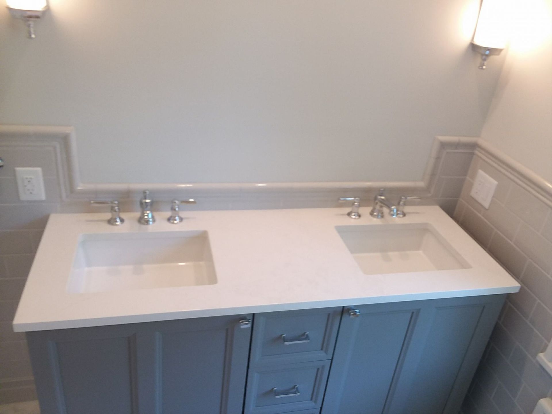 Gray double sink vanity with white countertop and sinks, mounted under a wall with sconces.