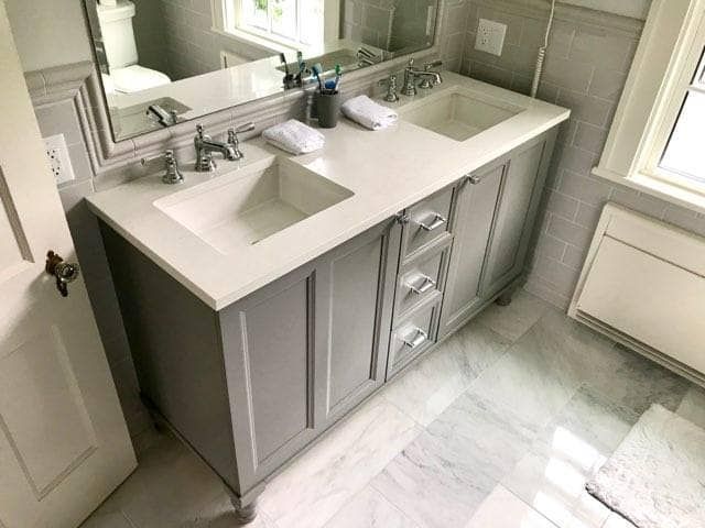 Gray bathroom vanity with double sinks, countertop, and drawers; mirror above.