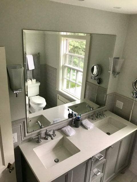 Bathroom with a double vanity and large mirror. Gray walls, white countertops, and a toilet.