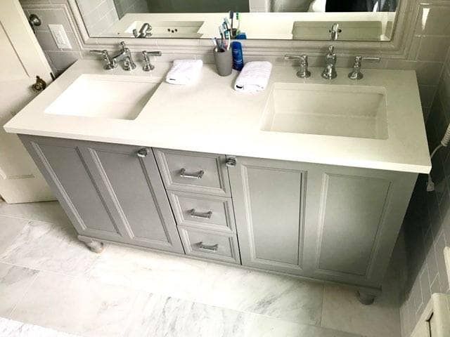 Gray double bathroom vanity with white countertop, sinks, and towels. Marble floor.