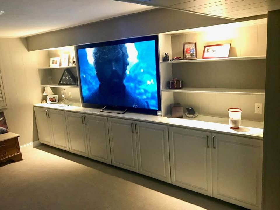 Built-in white cabinets and shelves with a large TV mounted in the middle. Warm lighting illuminates the space.