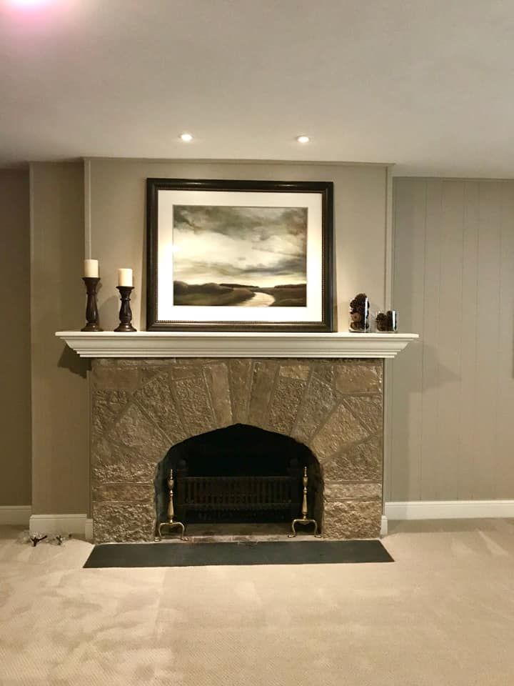 Stone fireplace with dark framed artwork and two candle holders.