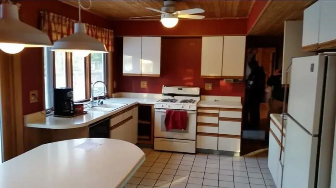 Kitchen with white cabinets, appliances, and island; red walls, wood ceiling, and tile floor.