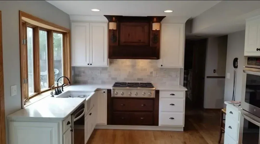 Kitchen with white cabinets, dark wood range hood and window trim, and light countertops.