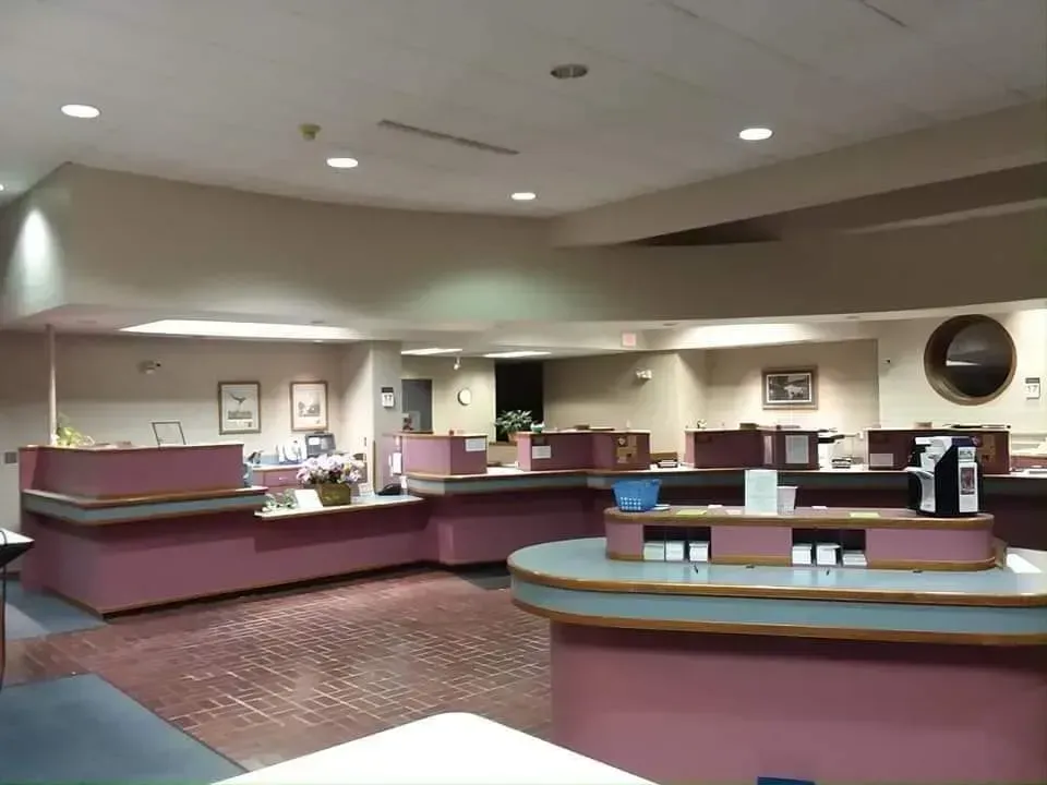 Interior of a bank with several pink counters. Brick floor, neutral walls, and a coffee machine.