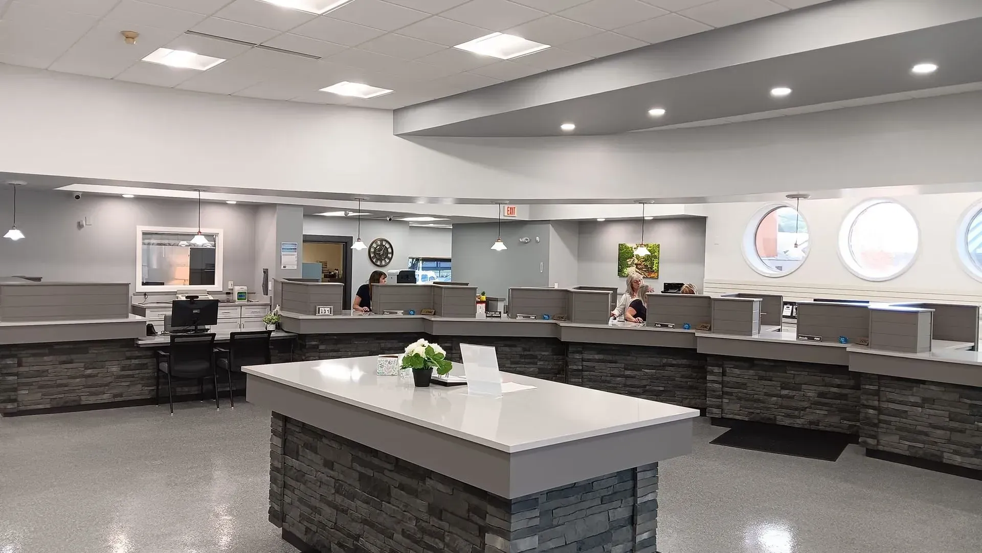 Bank interior with teller stations and a central desk. Light gray and stone-colored accents.