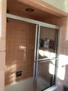 Pink-tiled bathroom shower with sliding glass doors.  Soap and shampoo bottles visible.
