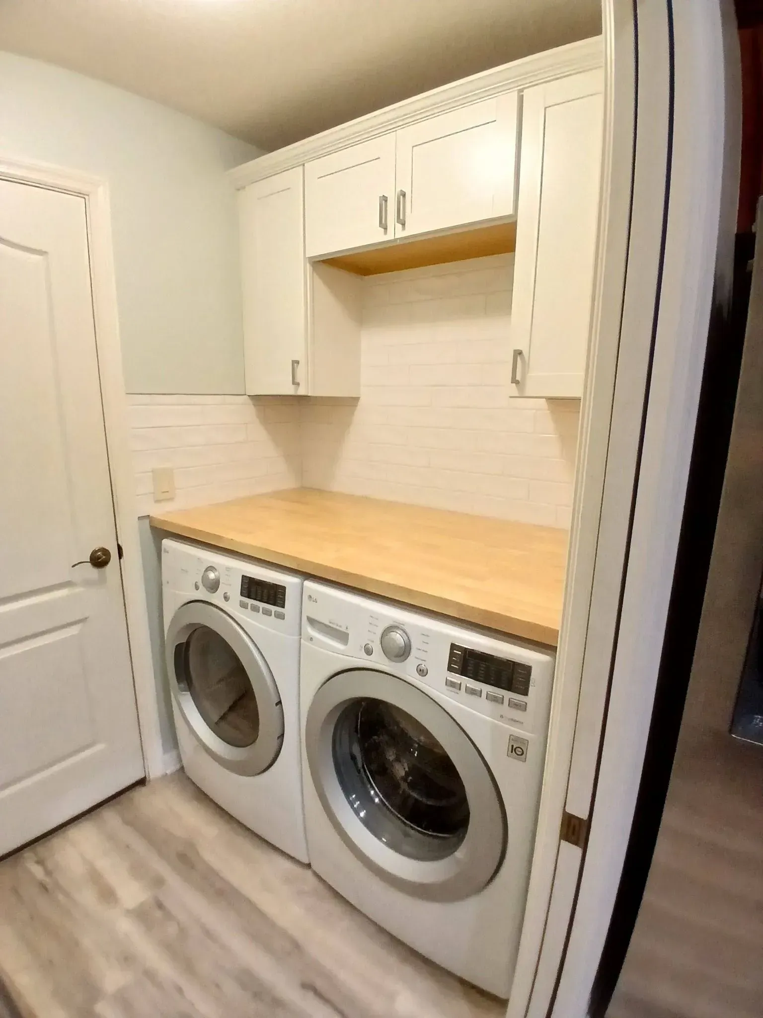Laundry room with white washer and dryer, cabinets, wooden countertop, and door.