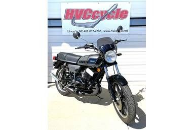 A vintage black Yamaha motorcycle parked on a concrete surface in front of a white garage door with an HVCycle sign.