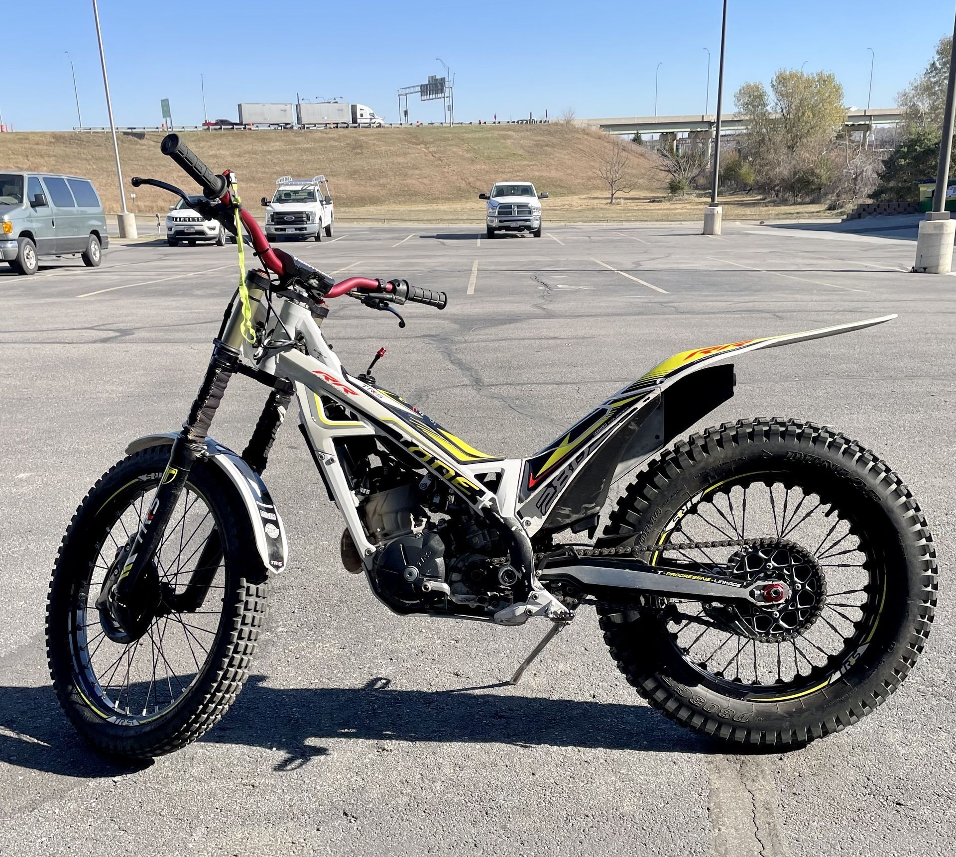 A Gas Gas trials motorcycle parked in an outdoor asphalt parking lot on a sunny day.