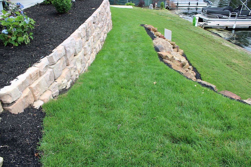 A lush green lawn with a stone wall and a boat in the background.
