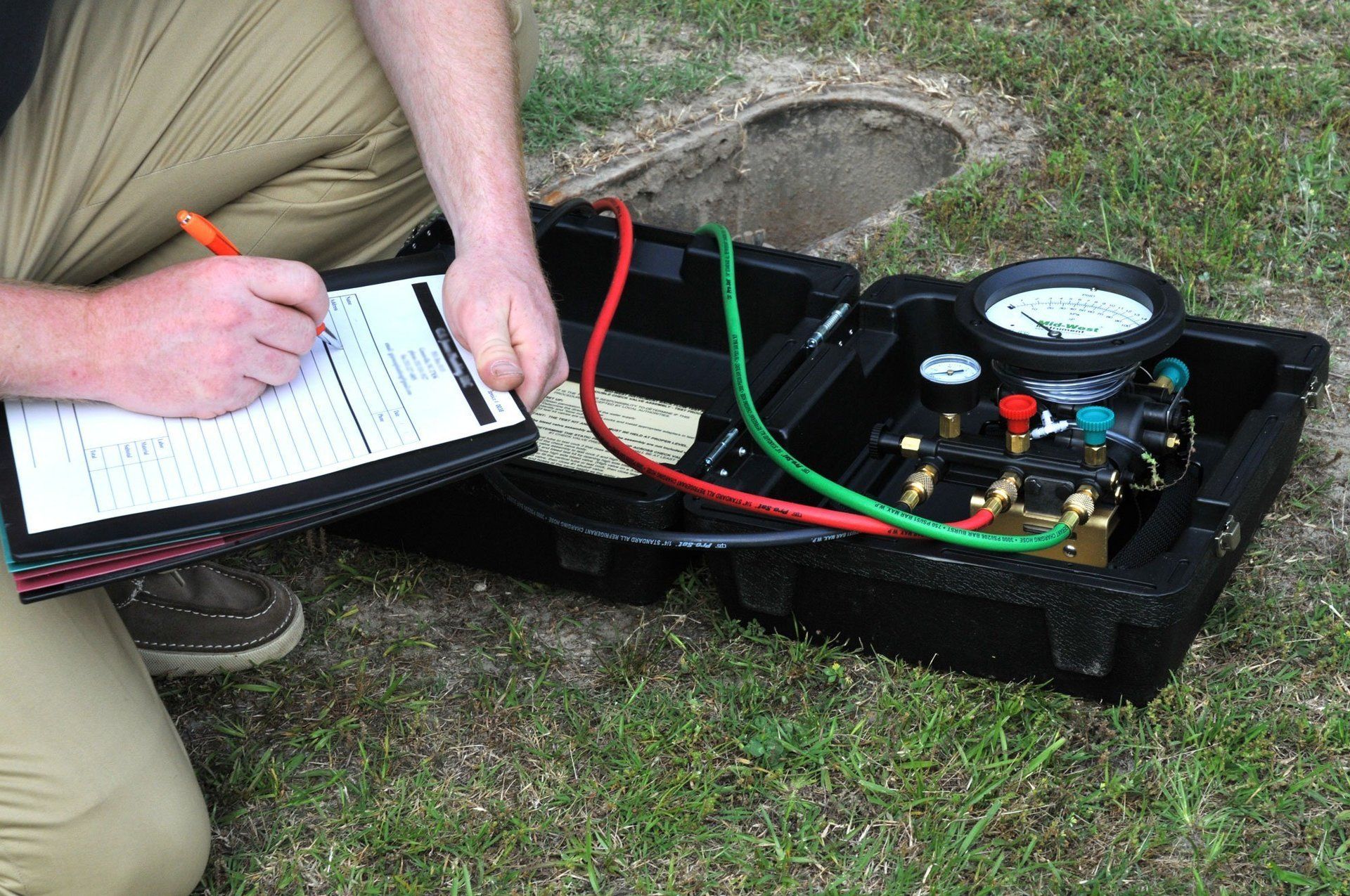 A man is writing on a clipboard next to a backflow test kit