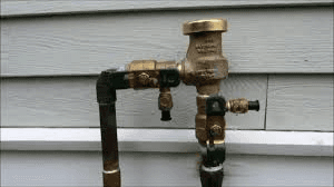 A close up of a water valve on a pipe outside of a house