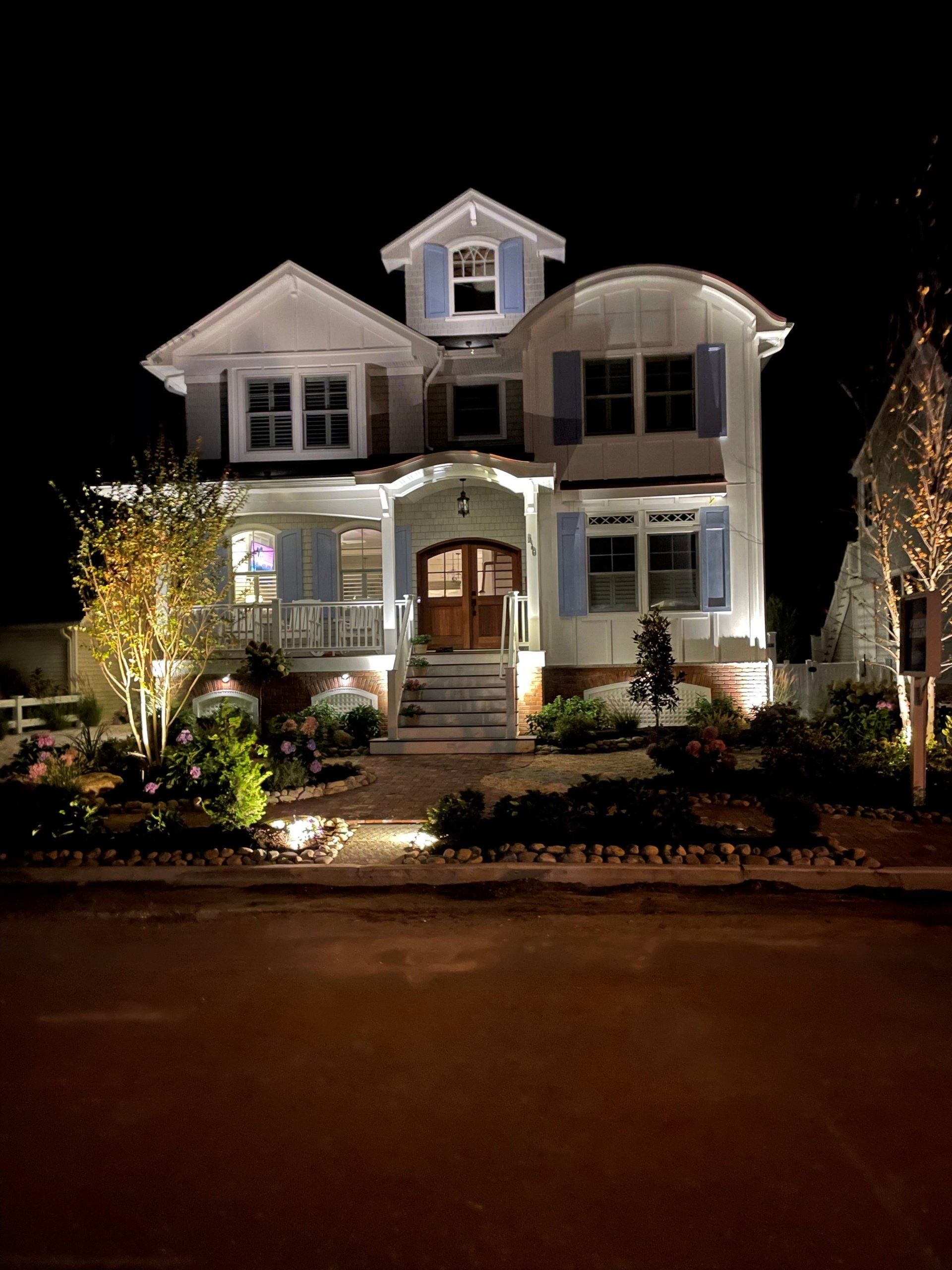 A large white house with blue shutters is lit up at night