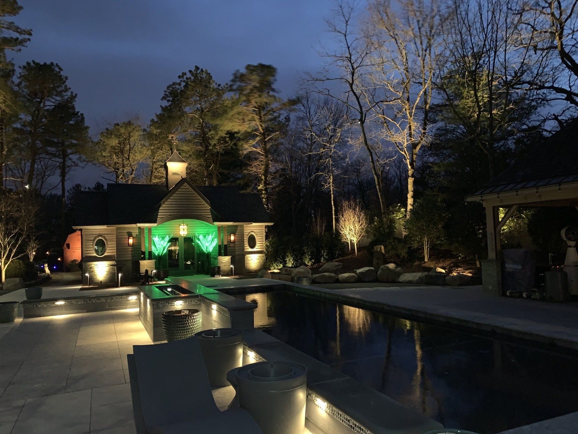 A well lit house with a pool in front of it