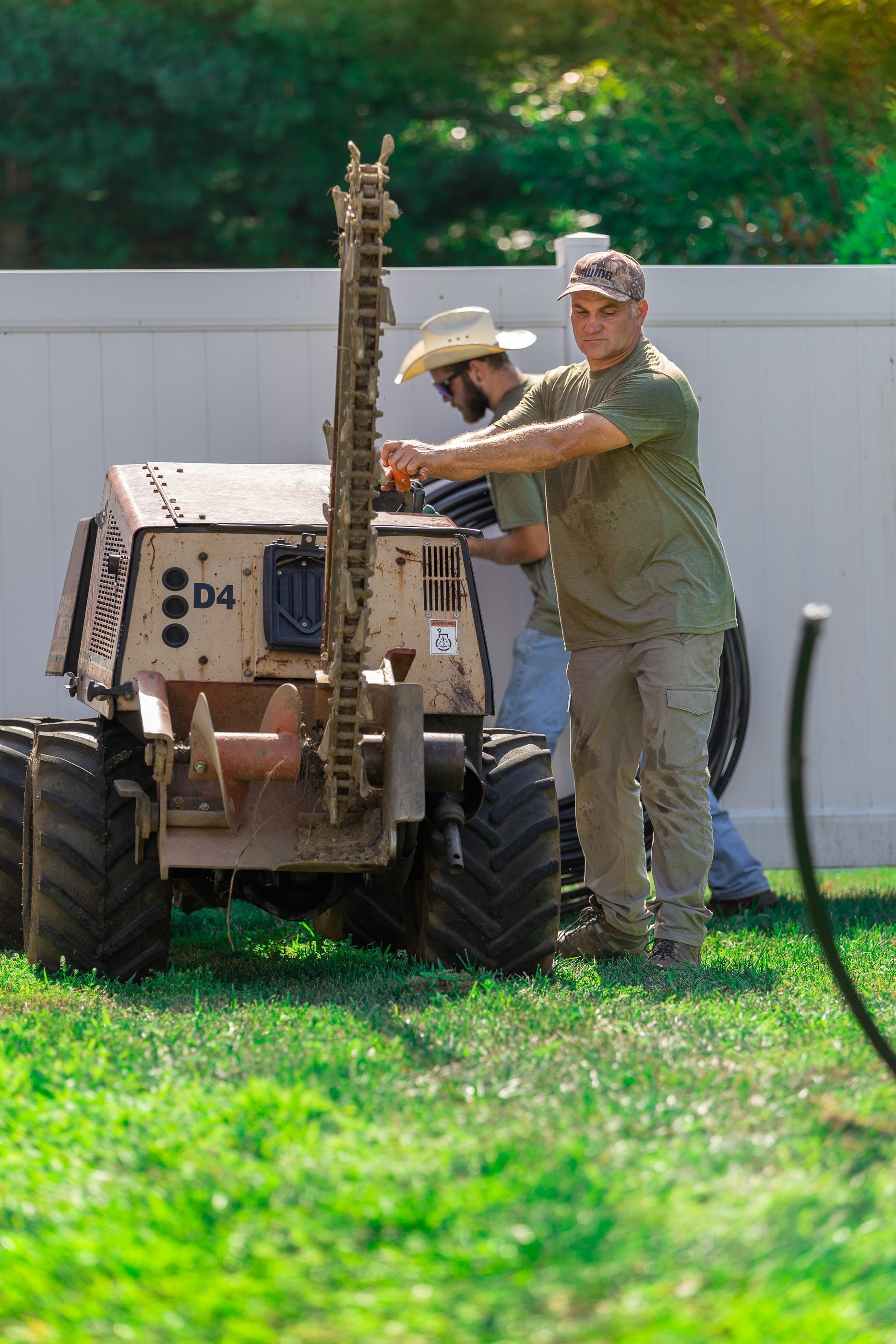 Two men are working on a trencher in a yard