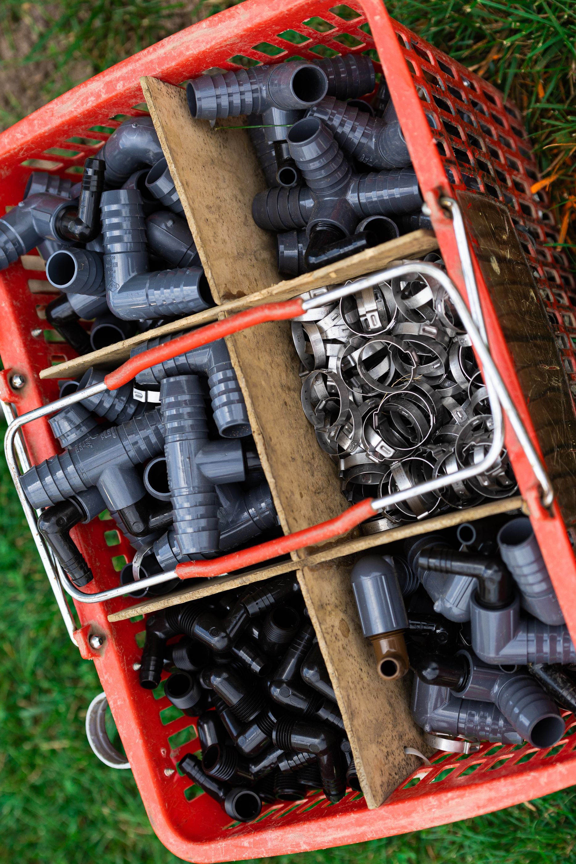 A red basket filled with pipes and fittings is sitting on the grass