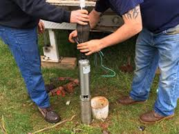 Two men are working on a water pump in the grass